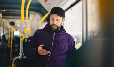 A man standing on public transport, he is looking at his phone