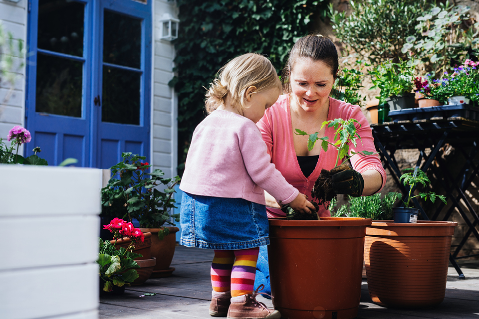 A mother and young daughter potting a plant in their back garden